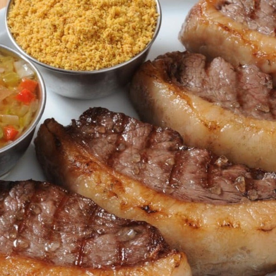 Descubra o sabor incomparável da nossa 'Picanha', um clássico da categoria 'Churrasco'. Servida em generosas porções de aproximadamente 450 gramas, a picanha selecionada é suculenta, tenra e repleta de sabor. Para realçar ainda mais o paladar, acompanha um molho irresistível, que agrega um toque especial ao prato. E, para completar essa experiência gastronômica, uma farofa crocante e deliciosamente temperada. Uma combinação perfeita para os amantes da culinária brasileira.