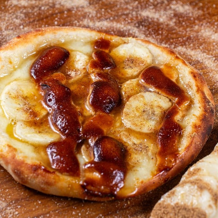 """Esfiha Banana Nevada: Uma esfiha doce irresistível, recheada com banana madura, polvilhada com açúcar e canela, e finalizada com uma camada de leite condensado que ""Esfiha Banana Nevada: Uma esfiha doce e deliciosa, recheada com banana madura e polvilhada com uma generosa camada de açúcar e canela. Com sua massa levemente crocante, essa esfiha oferece um toque aconchegante e irresistível a cada mordida, perfeita para os amantes de sobremesas suaves e saborosas!""cria o efeito nevado. Uma sobremesa perfeita para quem busca doçura e aconchego em cada mordida!"""