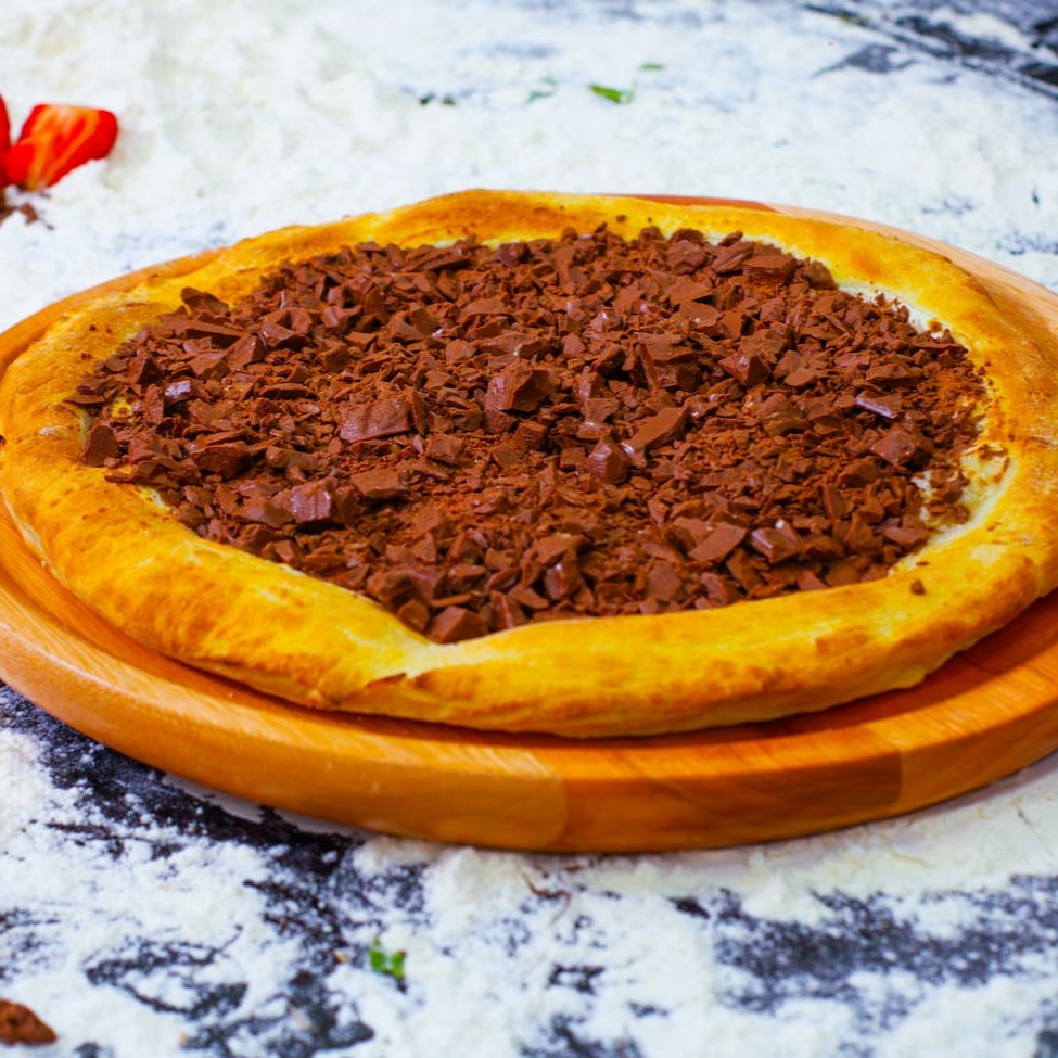Pizza Doce de 40cm, exuberantemente recheada para os verdadeiros amantes de chocolate. Esta pizza é tão generosamente preenchida que parece que você poderia iniciar sua própria fábrica de chocolate! Cada pedaço transborda com o mais puro chocolate Nestlé, criando uma experiência irresistível e deliciosamente lambuzante. Perfeita para satisfazer os desejos mais intensos de chocolate, nossa pizza é uma sinfonia de sabor que irá encantar o seu paladar.