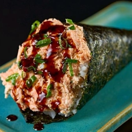 Temaki em formato de cone recheado com arroz e salmão grelhado, com creme cheese e cebolinha finalizado com tare e gergelim, na compra de um temaki ganha outro grátis .