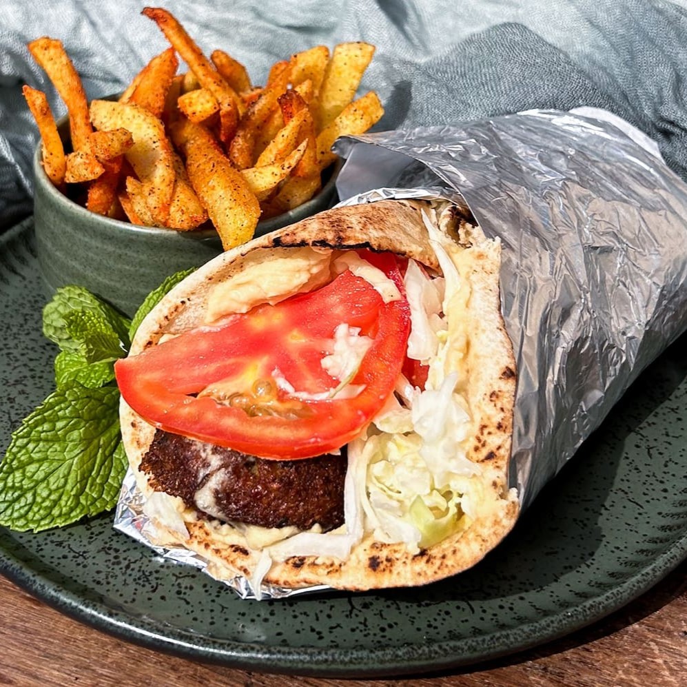 Sanduíche kebab de falafel crocante no pão pitta, com hommus tahine, molho tahine, salada de repolho com emulsão de alho e tomate. Acompanha batata frita da casa temperadinha
