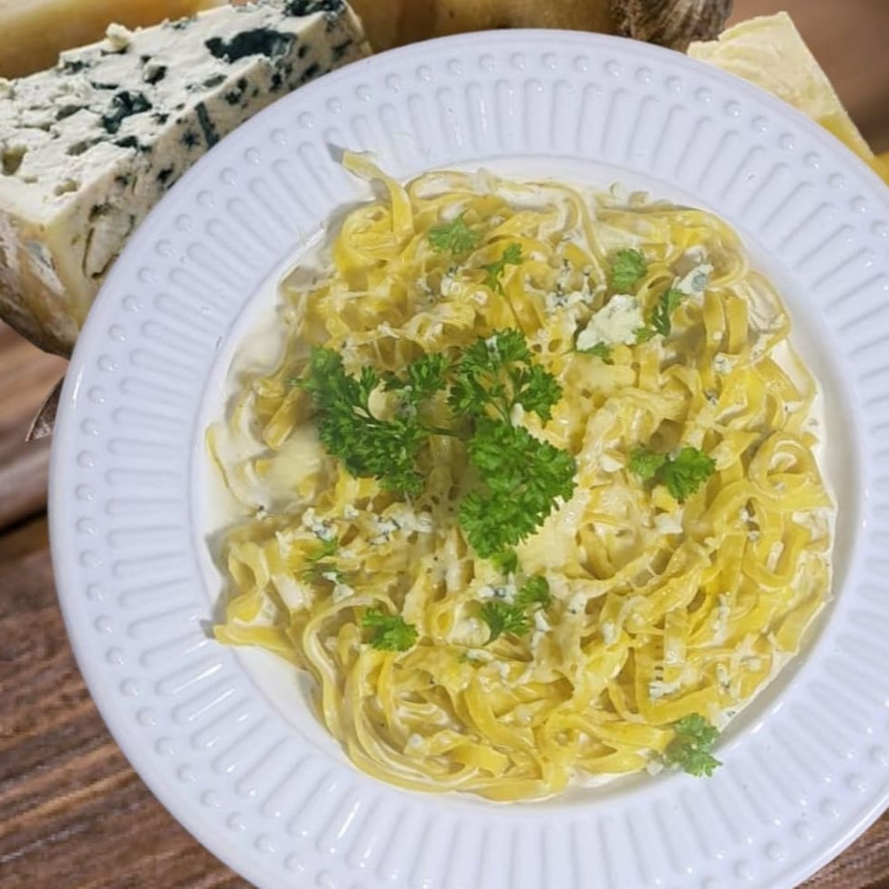 Nosso 'Fettuccine ai Quattro Formaggi' é uma irresistível combinação de sabores, que figura entre os mais pedidos. A massa de fettuccine, delicada e perfeitamente cozida, se une a um cremoso e encorpado molho à base de creme de leite. Este molho é enriquecido com uma seleção sofisticada de queijos: o queijo cremoso, que traz uma suavidade ímpar; o gorgonzola, famoso por seu sabor marcante; a muçarela, que adiciona uma textura incomparável; e o parmesão, que coroa o prato com seu toque final autêntico e robusto. Esta combinação resulta em uma experiência gastronômica inigualável, que encanta paladares e certamente irá te conquistar.