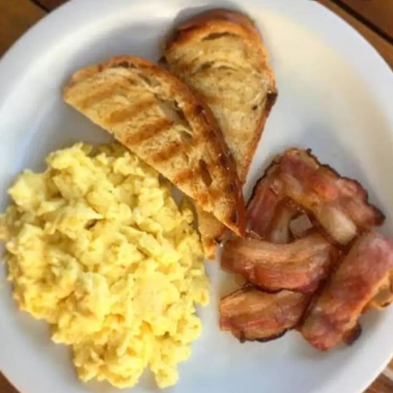 Porção generosa de ovos mexidos, bacon e torrada fresca