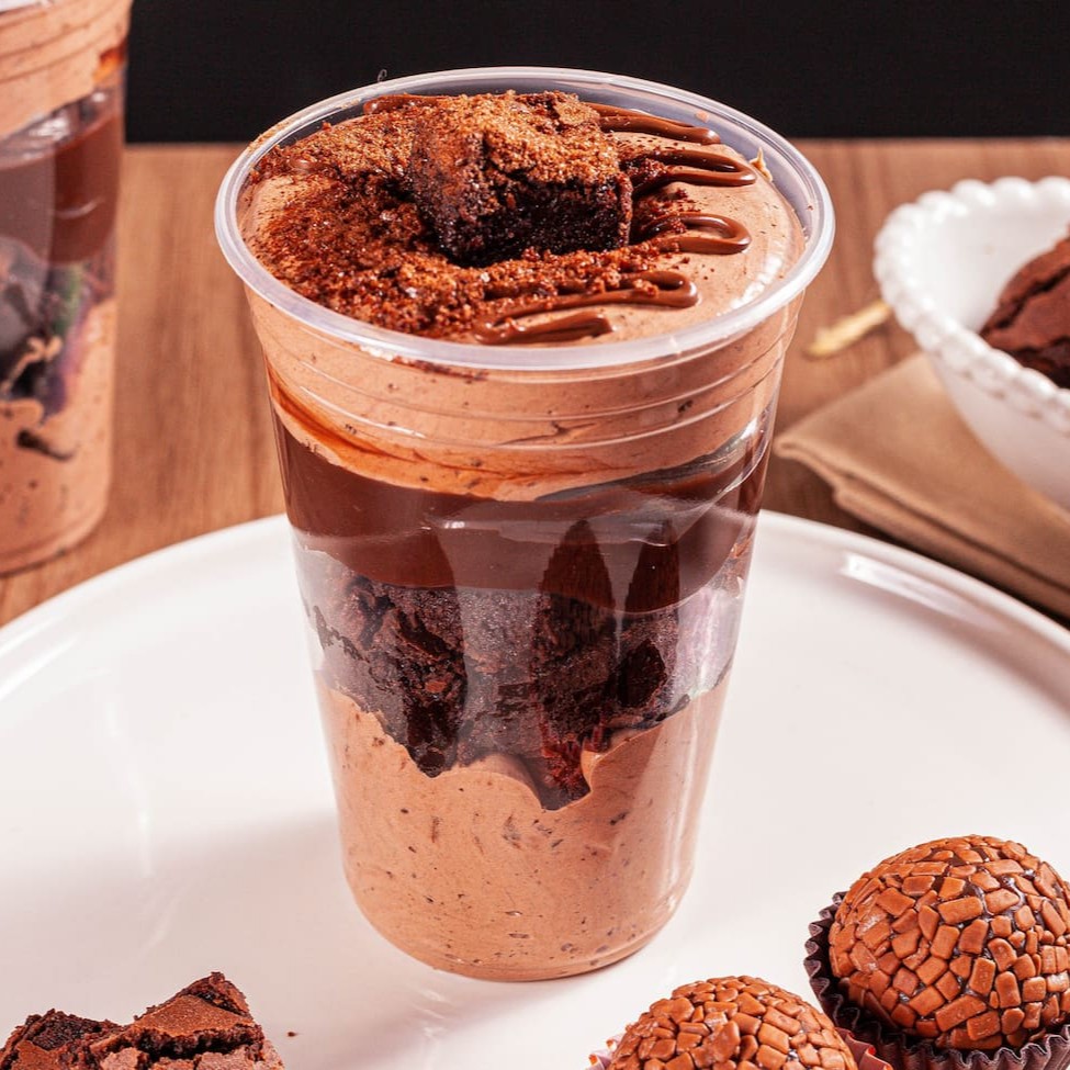 Prepare-se para uma aventura de sabores com o Copo Mousse de Ovomaltine. Mousse de Ovomaltine, brownie, brigadeiro de chocolate cremoso e uma pitada de flocos de Ovomaltine, finalizados com fios de Nutella e pedaços de brownie, tornam cada colherada uma experiência crocante e indulgente.