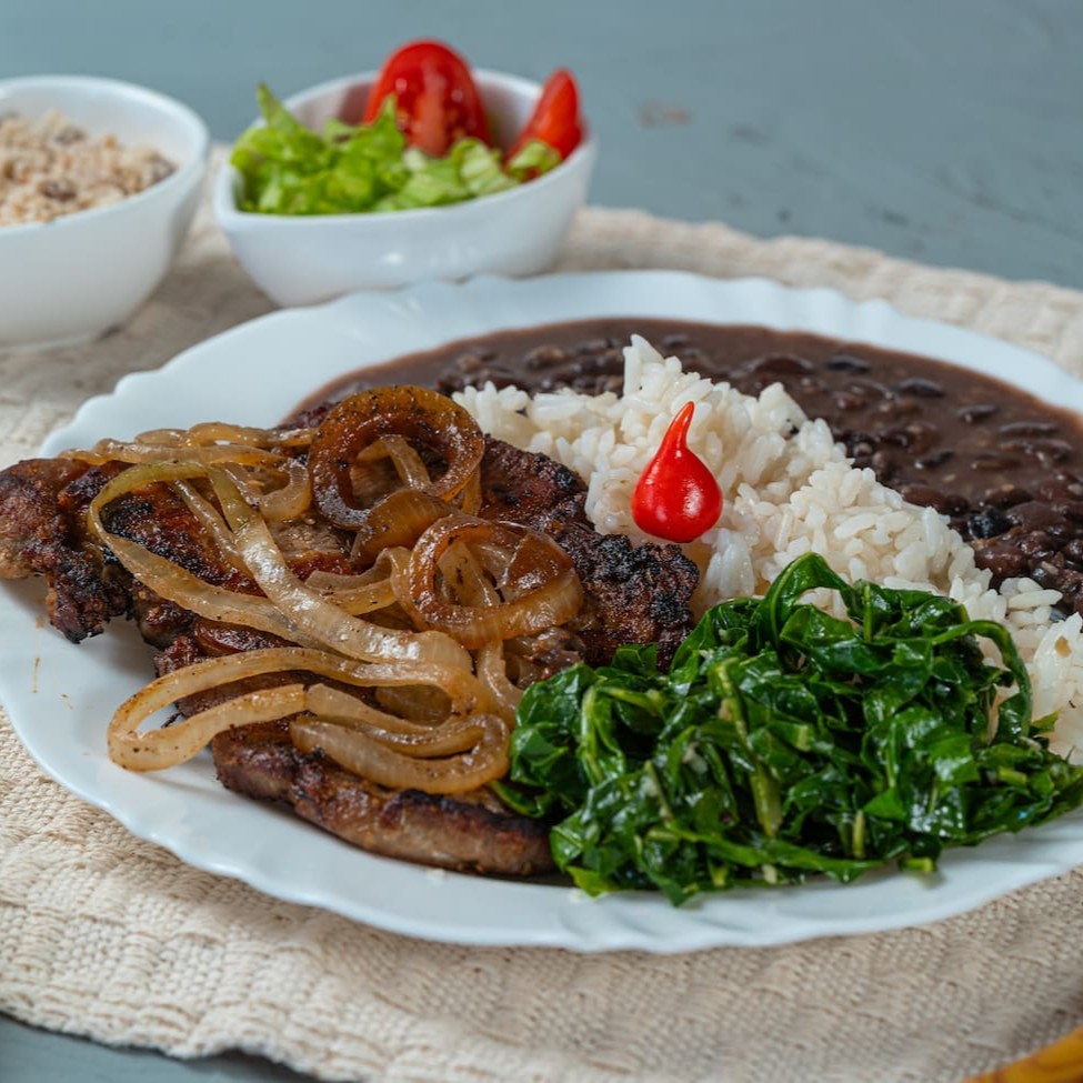 Bisteca suculenta grelhada no ponto perfeito, coberta com cebolas douradas e acompanhada de couve refogada bem temperadinha. Para completar, arroz soltinho, feijão caseiro, batatas fritas crocantes e farofa saborosa. Uma refeição cheia de sabor e tradição para matar a fome com qualidade!
