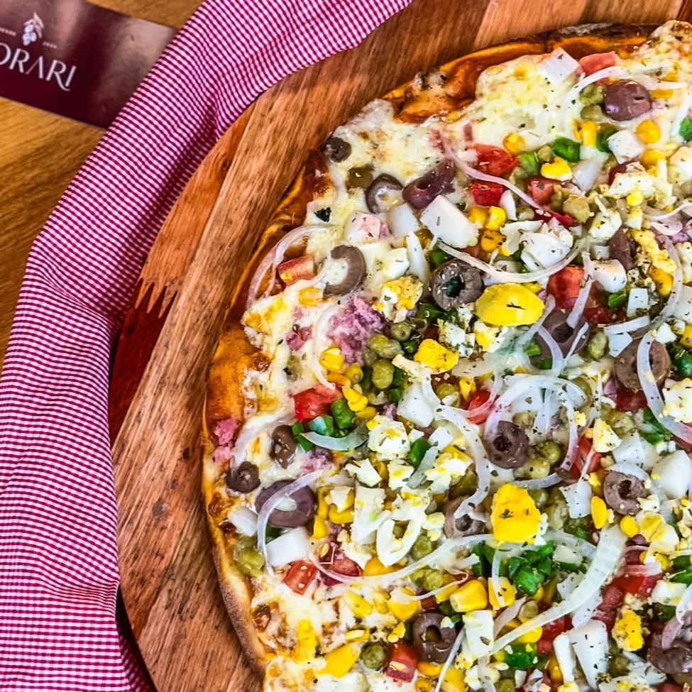 Molho da casa, mussarela, presunto, ovo, milho, ervilha, azeitona, palmito, cebola, pimentão e orégano.