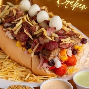 "Cachorro Quente -  1 Linguiça, molho '' cebola e tomate "" bacon, calabresa, presunto, muçarela, ervilha, milho, uva passas, azeitona, ovo de codorna, batata palha, queijo ralado, ketchup, maionese, mostarda e maionese temperada da casa."