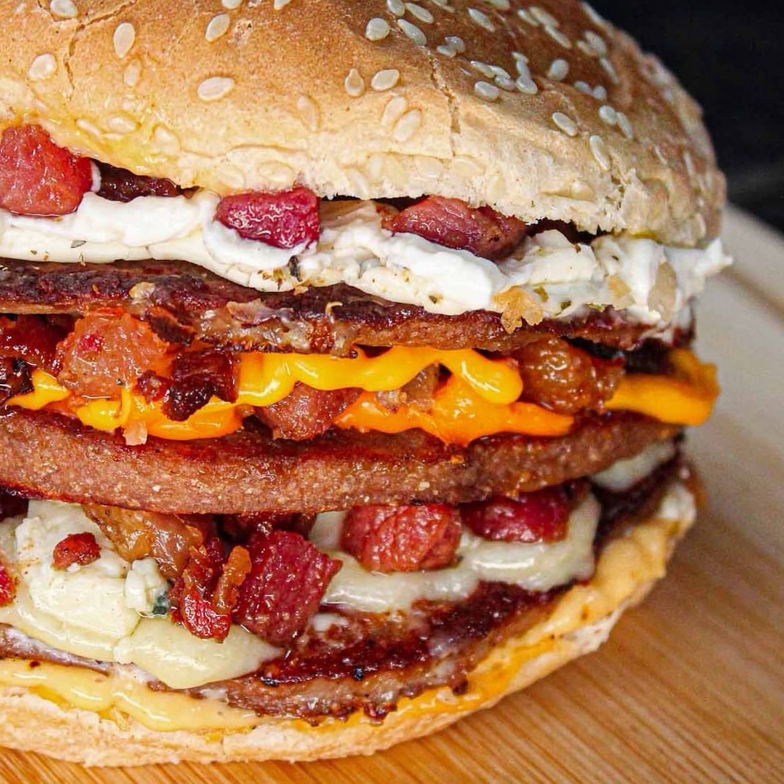 Pão com gergelim, 3 carnes, muçarela, gorgonzola, cheddar, Catupiry, bacon e molho