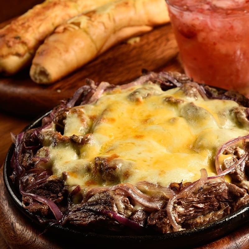 Filé mignon em tiras, acebolado e gratinado, coberto com mix de queijos e requeijão. Acompanha quatro mini deliciosos pães de alho.