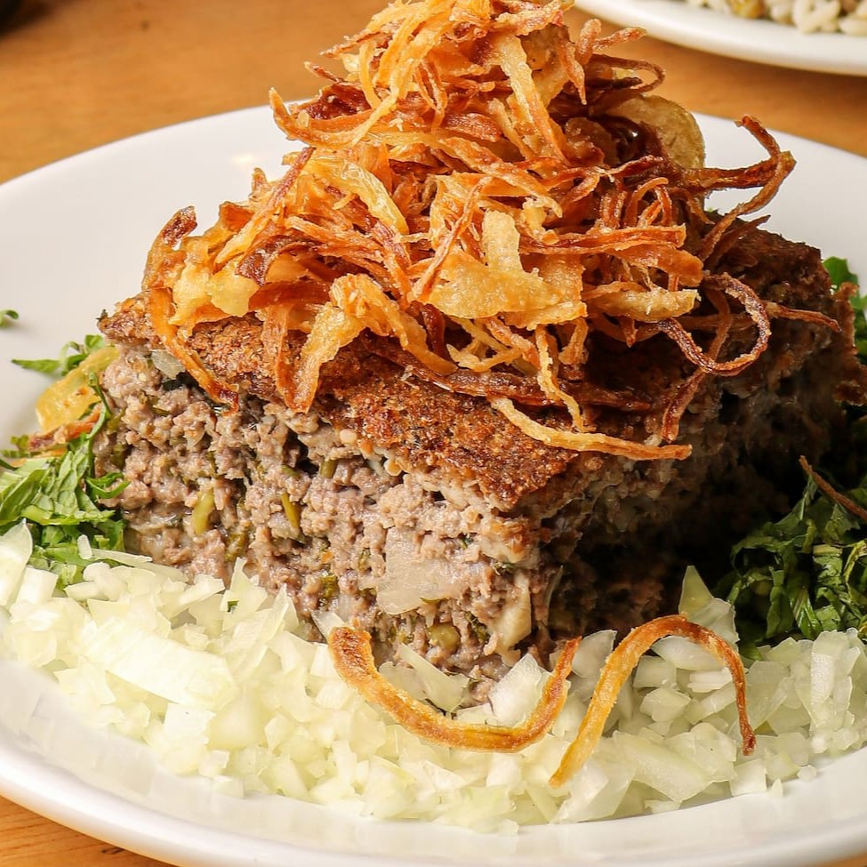 Delicioso quibe assado ao forno, recheado com carne bovina temperada com especiarias, acompanhado de cebola frita ou salsa e cebola picada