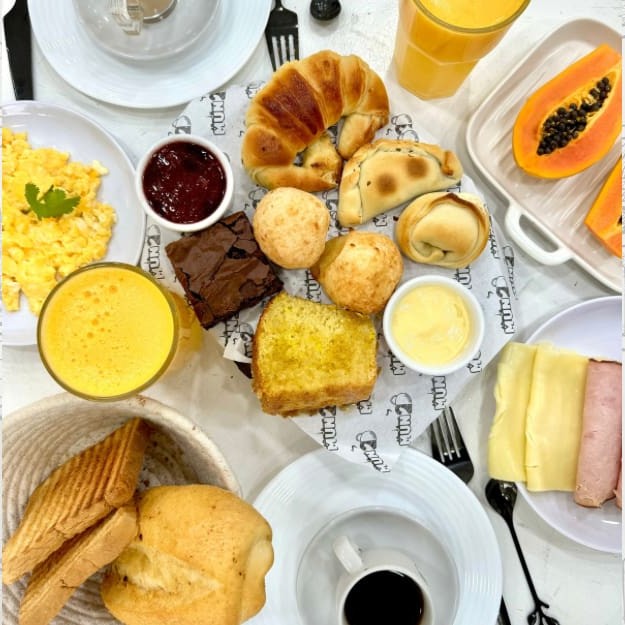 1 pão temperado •  2 pães de forma tostados • ovos mexidos • 2 fatias mussarela • 2 pedaços queijo minas • 2 fatias de peito de peru • geleia da casa • 1 medialuna • 2 mini empanadas argentinas • 1 fatia de bolo da casa • 1 Brownie • 2 pães de queijo • fruta da época • 2 sucos naturais de laranja de 300ml • 2 cafés