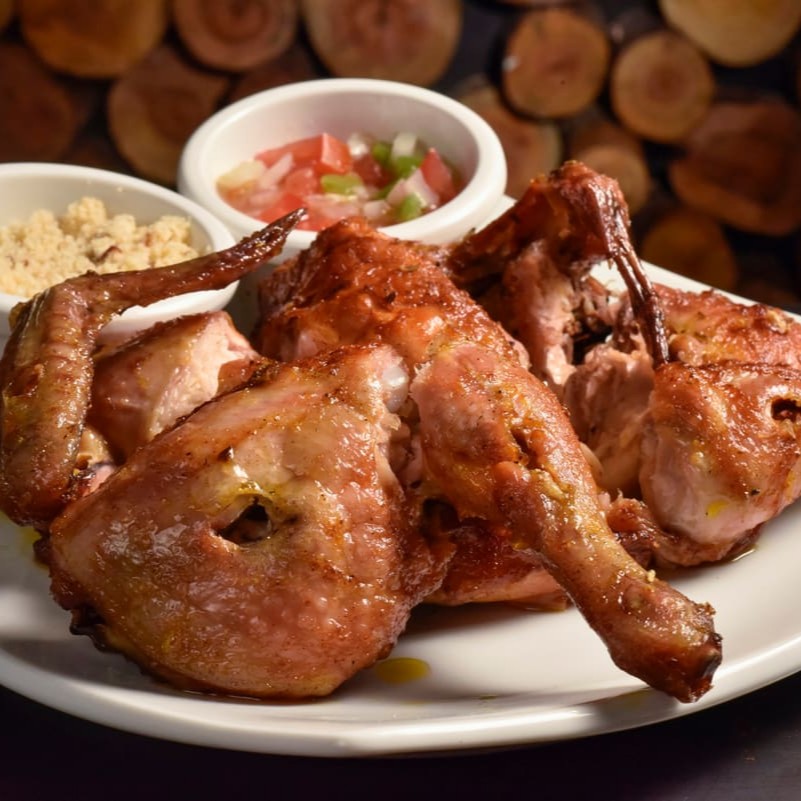 Suculento galeto assado na brasa, acompanha duas pequenas porções, um de farofa e uma de molho à campanha.