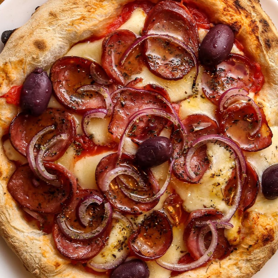 Pizza de longa fermentação com molho de tomate pelatti, muçarela, linguiça calabresa, cebola roxa, azeitona, orégano e fio de azeite. Tamanho médio: 28 cm