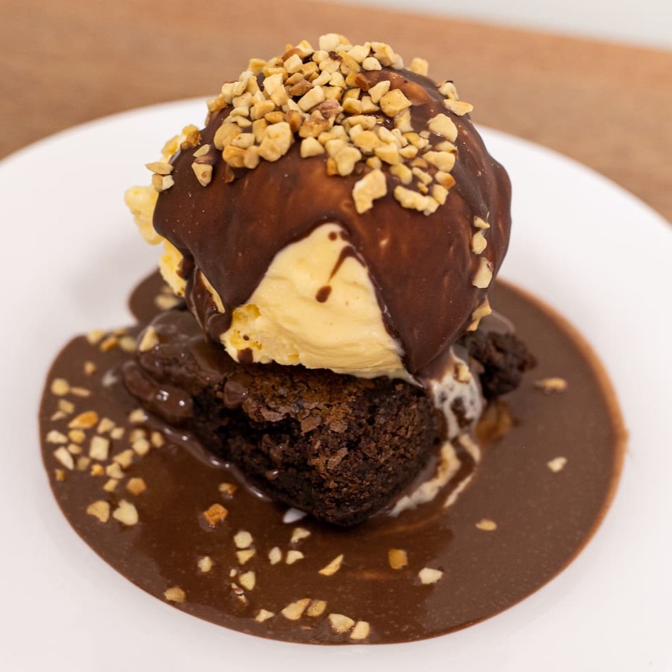 Este é o nosso cativante 'Brownie com Calda Quente', um destaque na nossa categoria 'Especiais'. Este prato inclui um brownie delicioso, harmoniosamente acompanhado por um sorvete cremoso. O sorvete é delicadamente coberto por uma camada crocante de chocolate tipo Skimó, proporcionando uma textura irresistível. O toque final é uma generosa porção de amendoim, adicionando um agradável contraste de sabor. Todos os componentes são enviados de forma separada em uma embalagem térmica, preservando a integridade e a frescura de cada item. Esta medida garante que você possa montar o prato e desfrutar da experiência culinária completa em casa. Por favor, observe que a foto é meramente ilustrativa. Acompanha sorvete de creme.