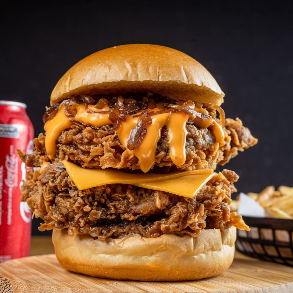 Aqui é pra quem tem fome de verdade! São 2 filés de sobrecoxa (ou 4 filezinhos crispy), queijo cheddar derretido, molho cheddar cremoso e cebola caramelizada, tudo no pão brioche. Acompanha batata P crocante e 1 bebida gelada. Grande, suculento e carregado de sabor — sem miséria!