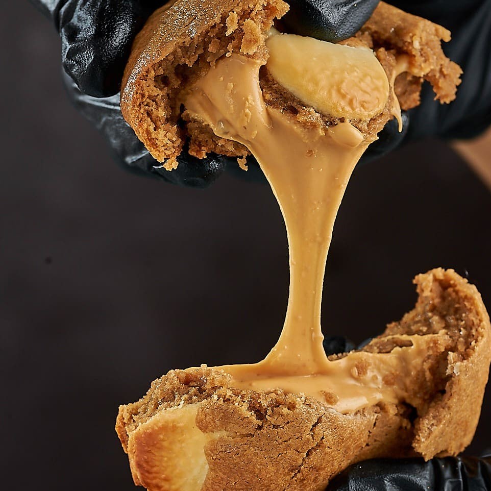 "Essa delícia combina gotas de chocolate branco com um recheio de chocolate branco assado para um sabor marcante, diferenciado e muuito delicioso! Importante: Os cookies de 100g não são gigantes ou ""monster"" como chamamos nossos cookies mais conhecidos, mas são tão deliciosos quanto e com sabores exclusivos!!"