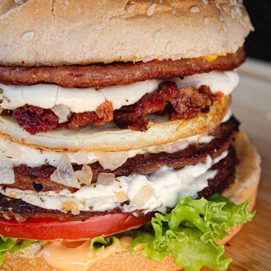 Pão com gergelim, 3 carnes, Catupiry, ovo, bacon, cebola, orégano, alface, tomate e molho.