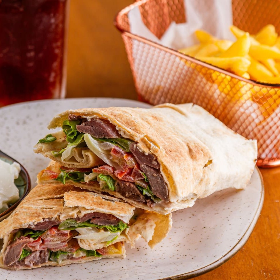 Nosso Shawarma de carne acompanha: Alface, tomate, cebola, salsinha e molho taratur ou Hommus Tahine + pasta de alho. Já vai com fritas! Escolha sua bebida e aproveite.
