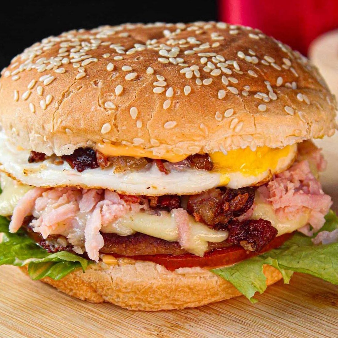 Pão com gergelim, carne, queijo, presunto, ovo, bacon, alface, tomate e molho