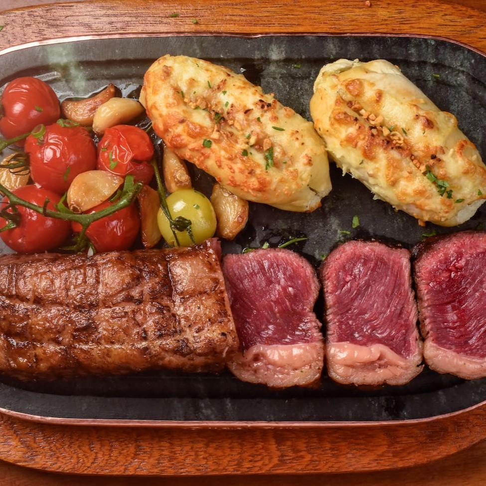 Clássico corte de Picanha (600g) e dois Pães de Alho Stadium. Acompanha Tomates e Cebolas Coquetel e Alhos Confit. Escolha dois acompanhamentos e um molho.