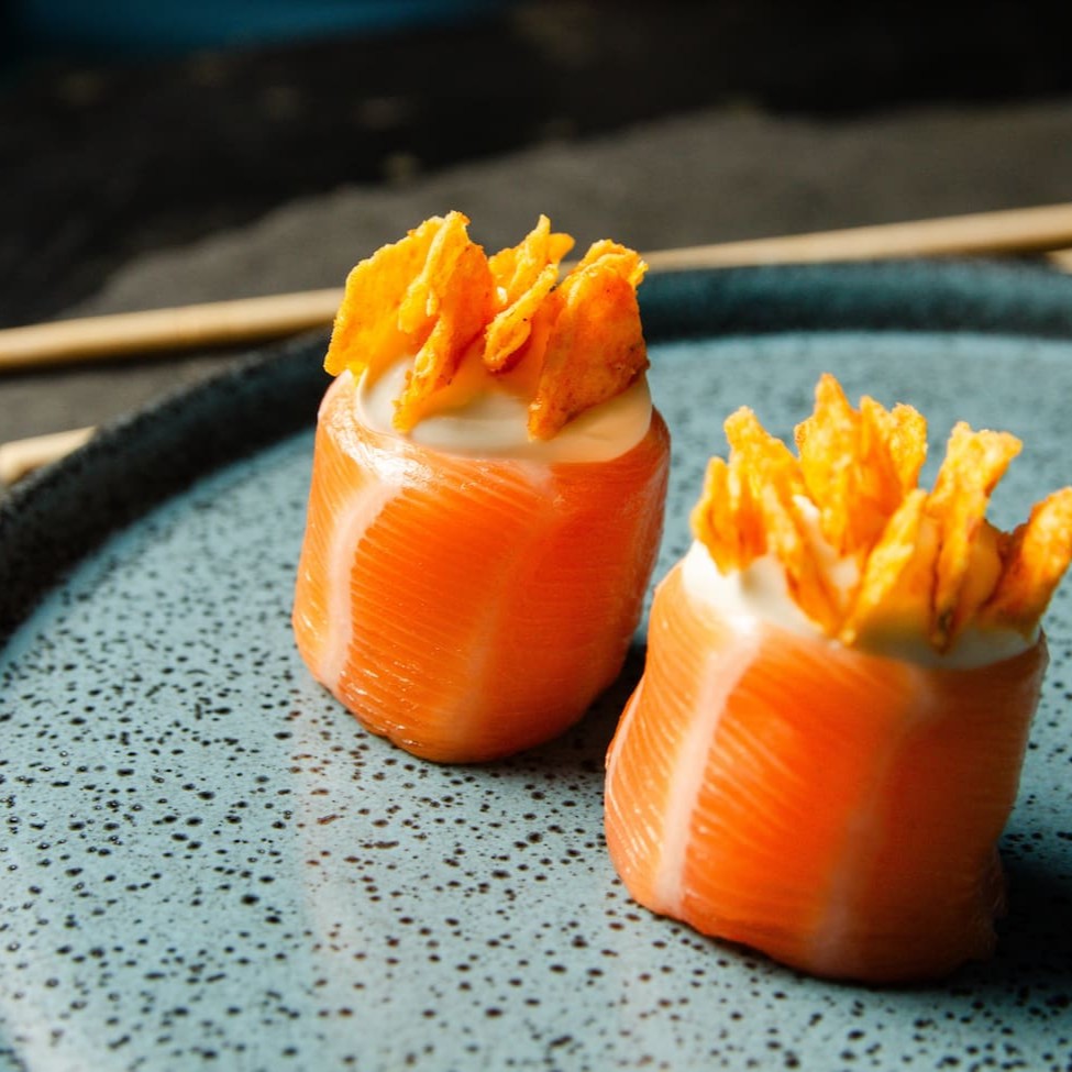 Salmão enrolando arroz com cream cheese e um toque de Doritos.