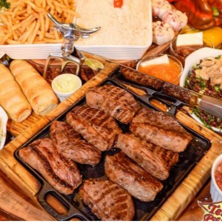 Delicie-se com o nosso '121 Bife Ancho Família para 4 Pessoas', um churrasco na pedra especialmente preparado para satisfazer paladares exigentes. Este prato é magnificamente composto por um suculento bife ancho, rico em sabor, acompanhado de um arroz bem temperado e um feijão tropeiro onde os sabores se fundem de maneira encantadora. Além disso, servimos irresistíveis batatas fritas crocantes, um molho caseiro e uma farofa de ovos que é a alegria do prato. Para completar, uma banana frita douradinha e um creme de alho especial com ervas finas que elevam o sabor a outro nível. Uma verdadeira festa de sabores para a família inteira!