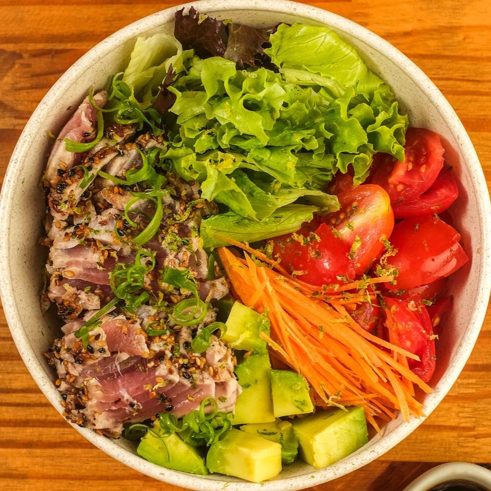 Base de quinoa, atum selado em crosta de gergelim, mix de folhas, gengibre fresco, tomate cereja, cenoura, abacate, finalizado com raspa de limão taiti e cebolinha. Acompanha Koa molho havaiano.