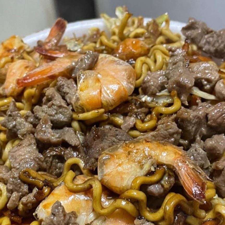 Este Yakisoba de Carne e Camarão é uma deliciosa combinação de sabores orientais. A carne suculenta e os camarões frescos e tenros são harmoniosamente misturados com cebolas crocantes, cenouras vibrantes e nutritivas, e uma mistura colorida e saborosa de repolho branco e roxo. Este prato é um verdadeiro desfile de cores, texturas e sabores, que certamente irá encantar o seu paladar. Cada garfada é uma experiência única e agradável, recheada de ingredientes frescos e de alta qualidade. Venha experimentar e se apaixonar por este nosso clássico da culinária oriental!