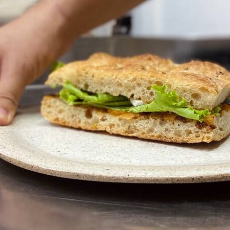 Fatias de focaccia artesanal e de longa fermentação, recheado com relish de tomate, fatias de tomate, alface e queijo azul vegetal