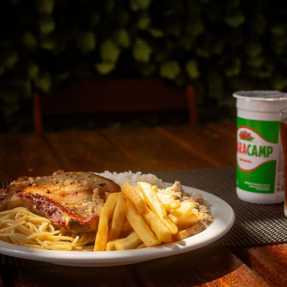 Um belo carrê suíno que vai acompanhado de  arroz branco, feijão preto, farofa temperada, macarrão e mais um complemento.