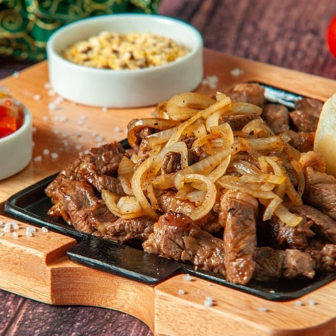 Generosa porção de Filé de alcatra cortado em tiras feito na chapa, acompanhado de uma porção de cebola refogada na manteiga para finalizar. Acompanha: Arroz, feijão, farofa e fritas dentro da marmita . Nossas refeições são ideais para uma pessoa. . Refeição servida e montada em uma marmita redonda de 750ml.