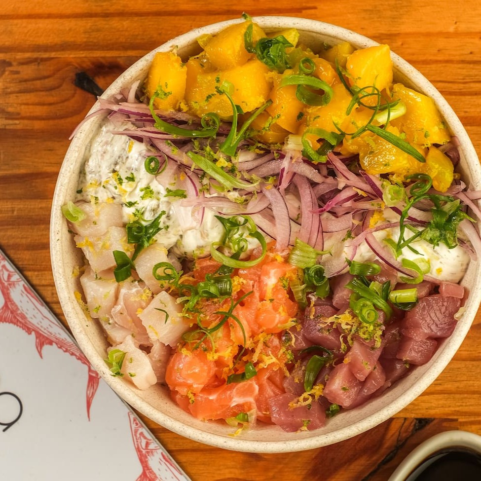 Base de arroz gohan, cubos de salmão, atum e peixe branco do Dia, Koa cream cheese (com nori), cebola roxa, manga, finalizado com raspa de cítricos e cebolinha. Acompanha Koa molho havaiano.