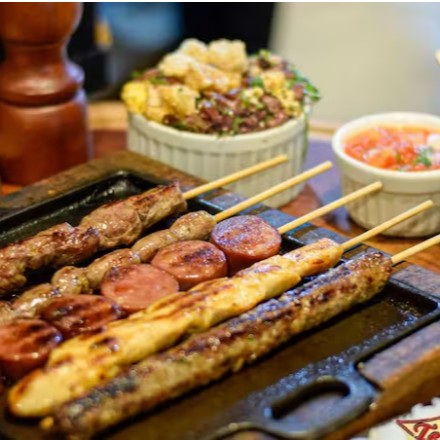 O '206 - Combinado 5 Espetos' é uma oferta especial para os amantes de espetinhos. Este prato, pertencente à categoria 'Espetinho na Pedra', é uma combinação sublime de espetinhos de boi, frango, porco, linguiça e coração, todos preparados à perfeição na pedra. Acompanhando os espetos, temos uma porção generosa de arroz, feijão e batatas fritas, crocantes e douradas. Para completar, uma farofa bem temperada e um molho caseiro dão o toque final a este festival de sabores. Viva uma experiência culinária única com o nosso '206 - Combinado 5 Espetos'.
