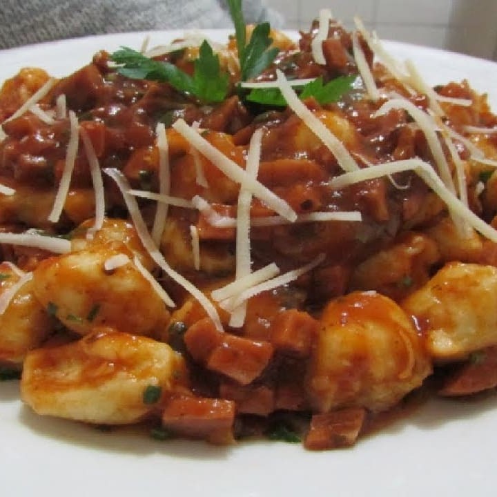Desfrute do nosso 'Nhoque de Calabresa ao Pomodoro'. Uma deliciosa iguaria artesanal, confeccionada com Batata Asterix de qualidade superior, meticulosamente envolvida em um saboroso e autêntico Molho Pomodoro. A Linguiça Calabresa Defumada, cortada em cubos, adiciona um sabor inigualável que se entrelaça harmoniosamente ao prato. O toque final é uma camada de queijo suavemente derretido e gratina