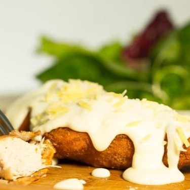 Bife de filé de frango empanado ao molho branco por cima, finalizado com  uma cobertura de queijo mussarela derretido.  Marmita composta por arroz branco, feijão preto, farofa da casa, mais um acompanhamento a escolher.