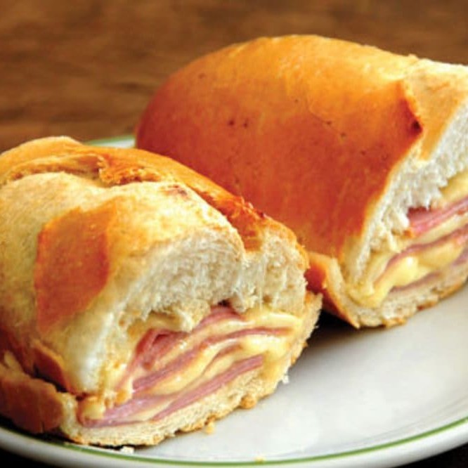 Deliciosa combinação de um clássico lanche brasileiro: o Misto Quente. Este saboroso sanduíche é preparado com um pão francês crocante por fora e macio por dentro, recheado generosamente com queijo prato derretido e fatias suculentas de presunto, tudo isso levado à chapa para alcançar o ponto perfeito de sabor e textura. Um lanche rápido, versátil e deliciosamente reconfortante que cativa o paladar a qualquer hora do Dia.
