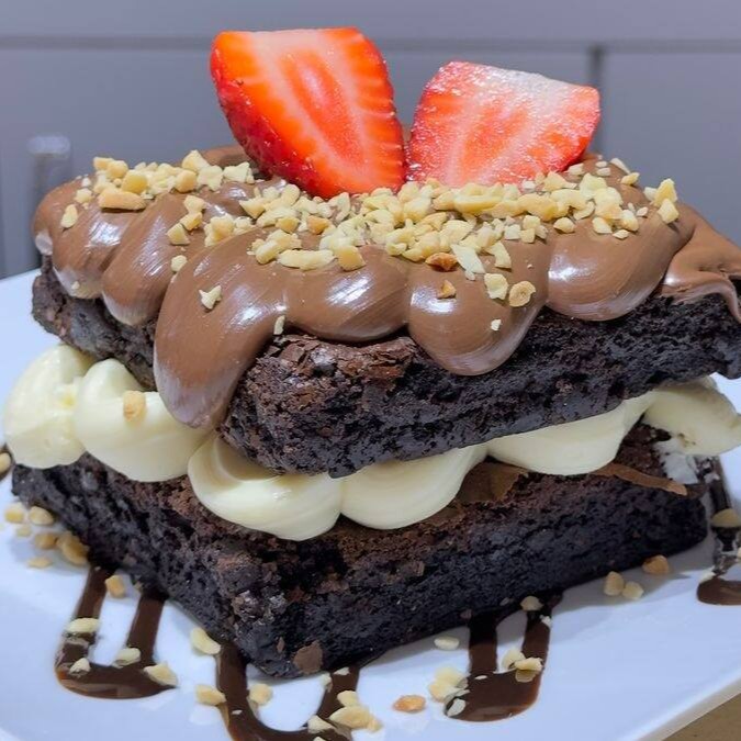 Delicie-se com nosso irresistível brownie de chocolate, coberto com um cremoso creme de Ninho e Nutella, salpicado com amendoim crocante e finalizado com um suculento morango. Uma explosão de sabores que vai adoçar o seu Dia!