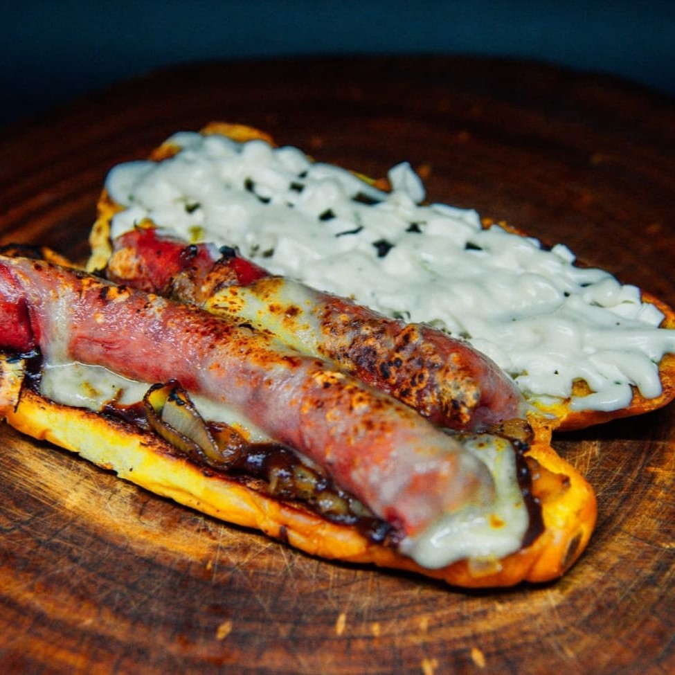 Pão Baguete de Alho c/ Parmesão, Linguiça Mineira, Queijo Gratinado, Cream Cheese, Maionese temperada da Casa e Cebola Caramelizada.