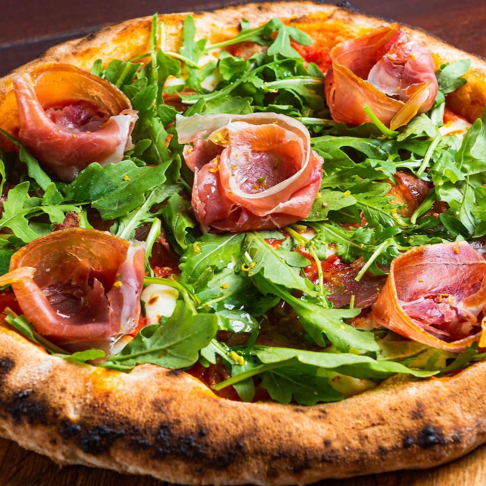 Massa em fermentação natural, molho de tomate, presunto de parma, mozzarela de búfala, raspas de limão siciliano, pistache, azeite trufado e rúcula