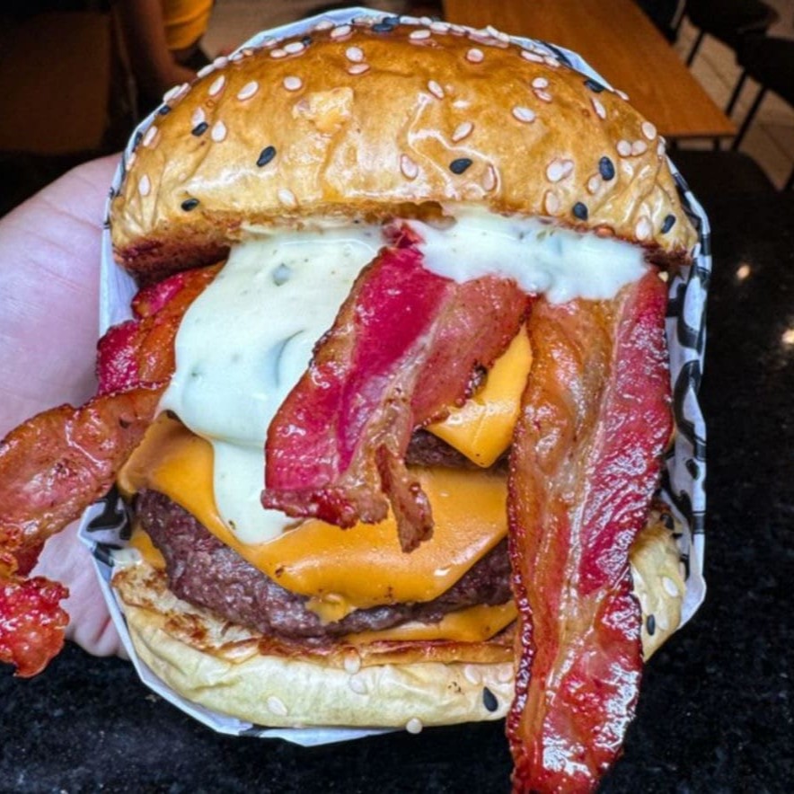 Três não é demais! Diferenciado pão com gergelim supremo selado na manteiga, Três blends 110g com queijo cheddar derretido no vapor, bacon fatiado crocante e a maionese verde do seu larica!