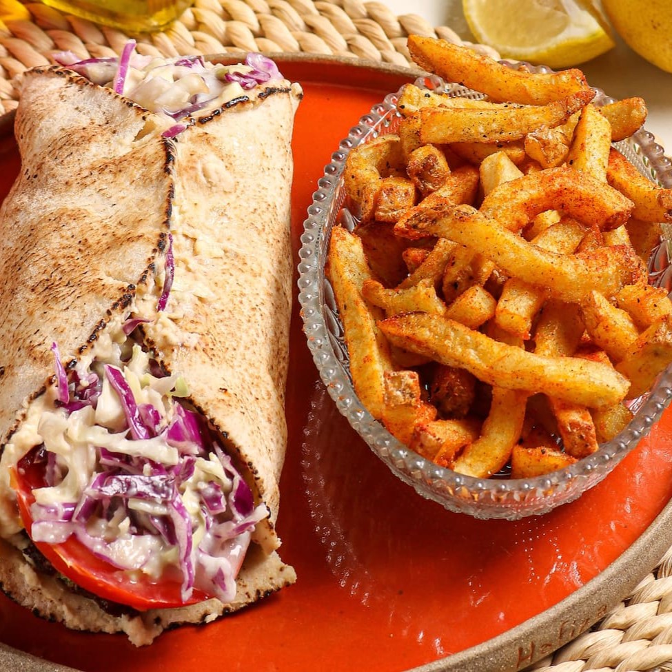 Sanduíche de filé de frango marinado na coalhada e especiarias no pão pitta, com hommus tahine, salada de alface e tomate com emulsão de alho. Acompanha batata frita da casa temperadinha e crocante