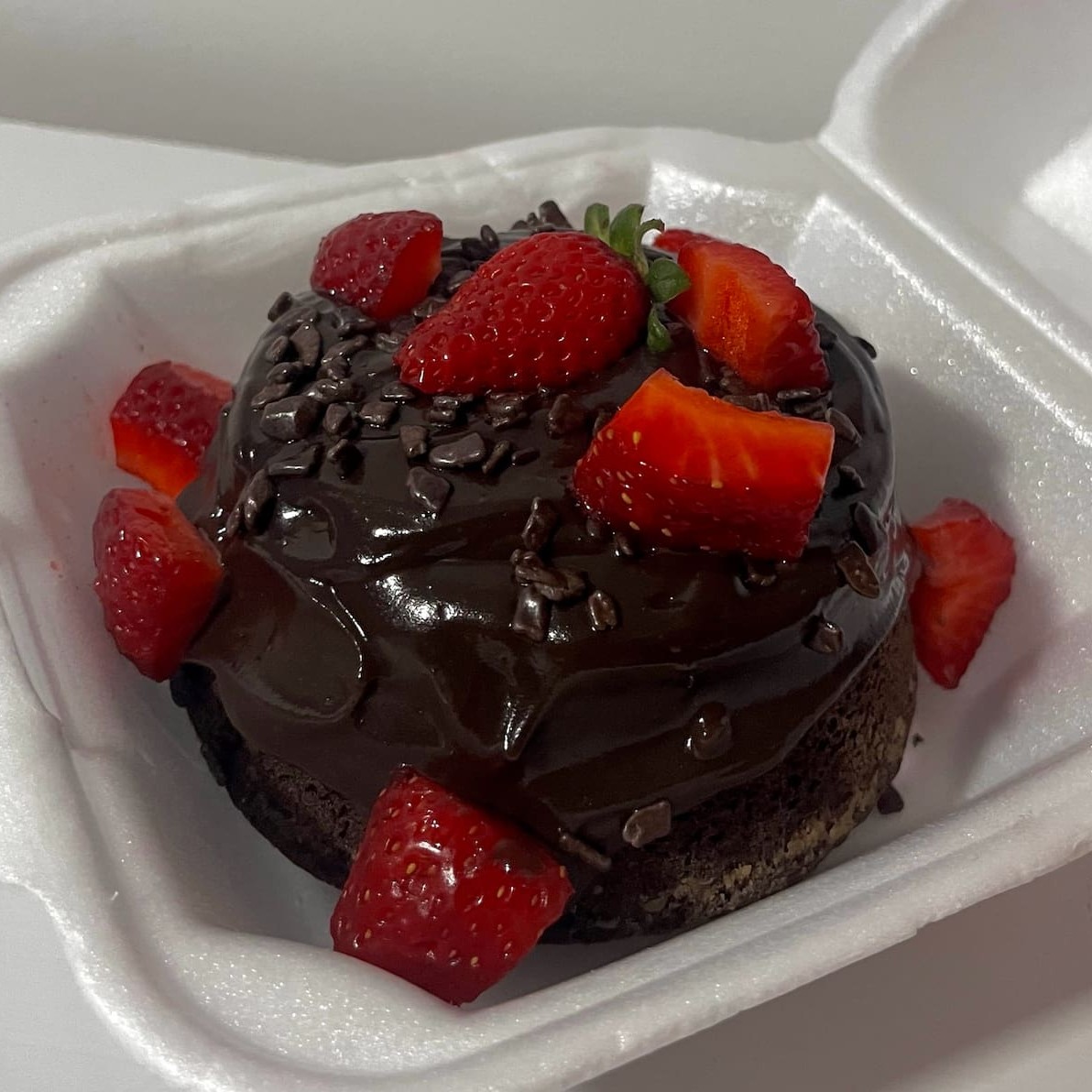 Delicioso bolo de chocolate com morangos cortados no meio e brigadeiro por cima.