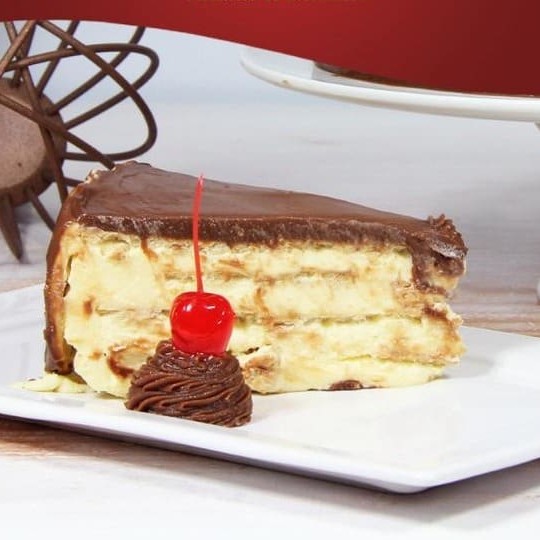 Deliciosa fatia de pavê Alemã feita com um leve creme de baunilha intercalado com biscoito tipo Maria com cobertura de chocolate.