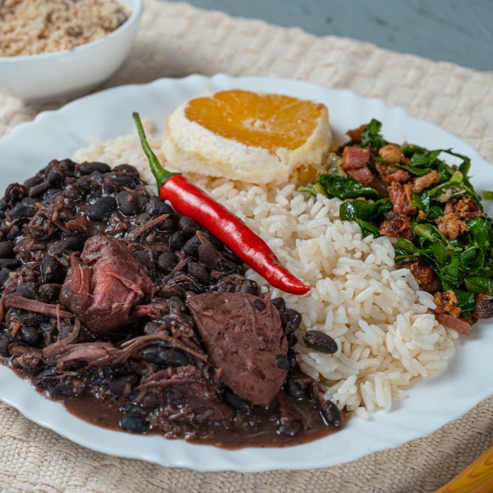 A clássica feijoada brasileira, preparada com carinho e ingredientes selecionados: carnes defumadas e feijão preto cozidos lentamente até ficarem no ponto perfeito. Acompanha arroz soltinho, couve refogada, farofa crocante e laranja fatiada para equilibrar os sabores. Uma explosão de sabor e tradição em cada garfada!
