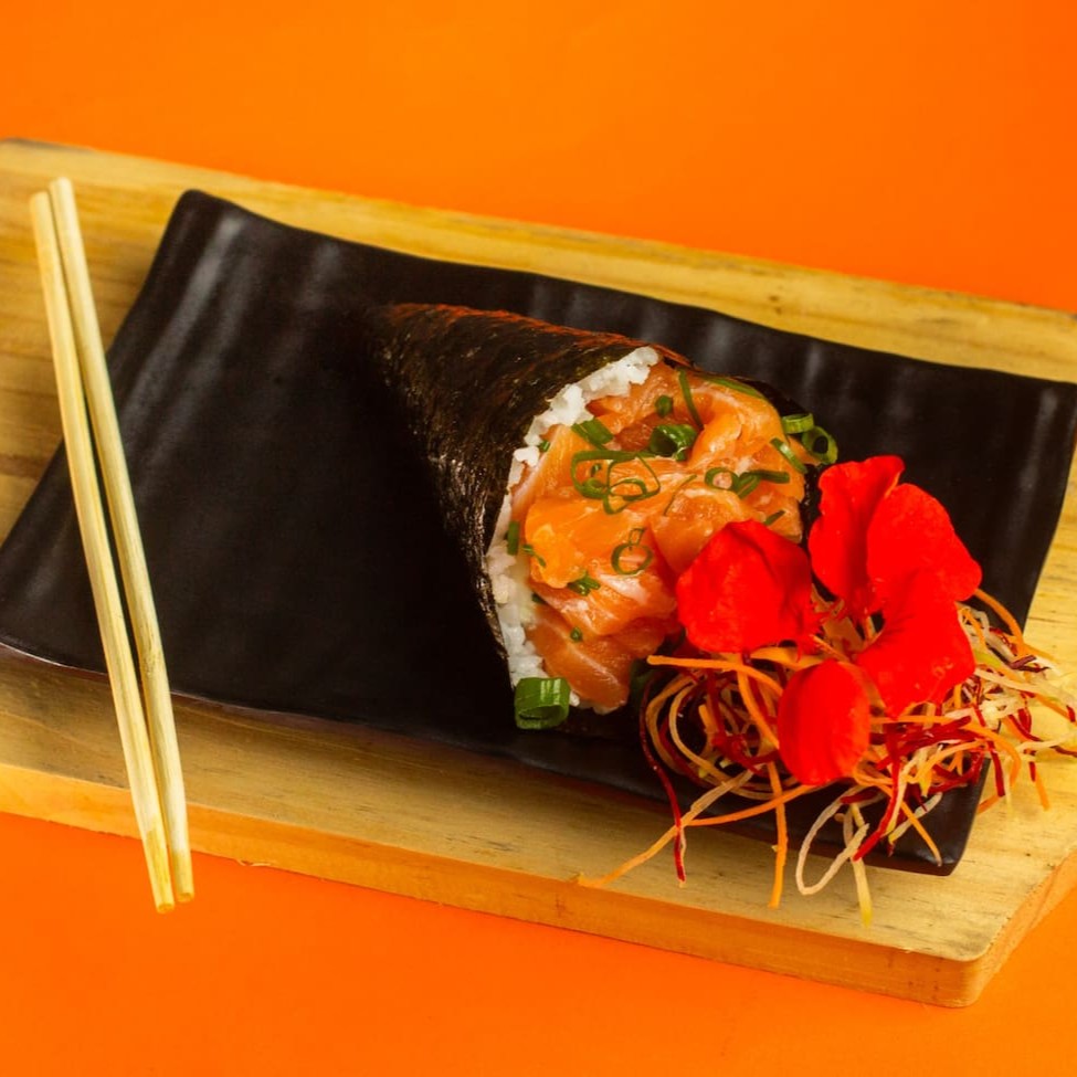 """Temaki Philadelphia preparado com alga crocante, arroz temperado no ponto certo e generosa camada de salmão fresco e suculento, combinada com o irresistível cream cheese que traz cremosidade e equilíbrio ao sabor. Enrolado na hora para garantir frescor e textura perfeitos, é uma explosão de sabores a cada mordida, ideal para os amantes da culinária japonesa."""