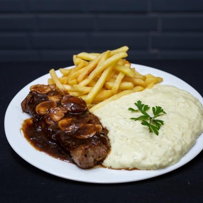Descubra a delícia do nosso 'Contra Filé ao Molho Madeira', o carro-chefe da casa.   Este prato é meticulosamente preparado com carne de alta qualidade, banhado num saboroso molho madeira caseiro e acompanhado de um delicioso arroz à piamontese.   Para garantir a qualidade de cada componente, eles são cuidadosamente embalados em recipientes separados.   É um prazer gourmet em sua própria casa!