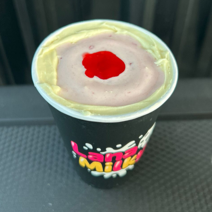 Sorvete cremoso batido com leite Ninho em pó, calda de frutas vermelhas. Chocolate branco na borda e cereja para finalizar