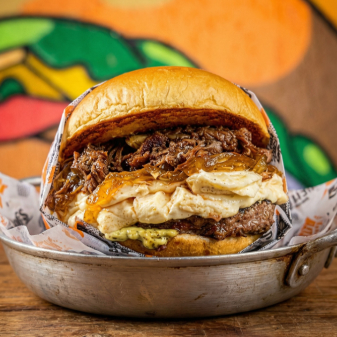 Pão brioche tostado na chapa com manteiga, hamburguer artesanal de aprox 160g, cream cheese, cebola caramelizada, costela cremosa desfiada e maionese da casa.
