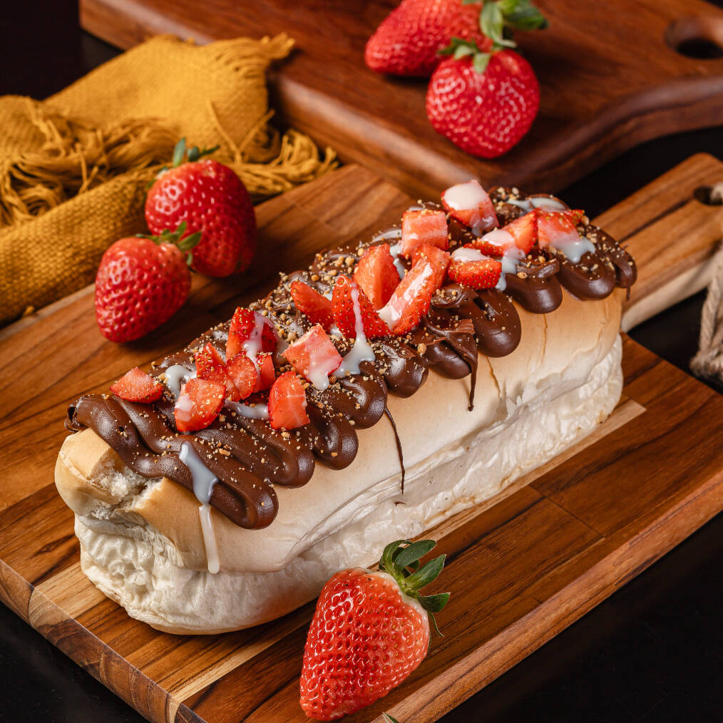 Pão macio Hot Dog, leite condensado, Morango, Farofa de amendoim, Bolinhas de chocolate crocante e chocolate preto derretido. Prensado.