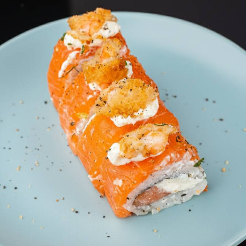 Uramaki de Salmão cobertas por manta de salmão maçaricado, com camarão crocante por cima, finalizado com gergelim moído e cebolinha.